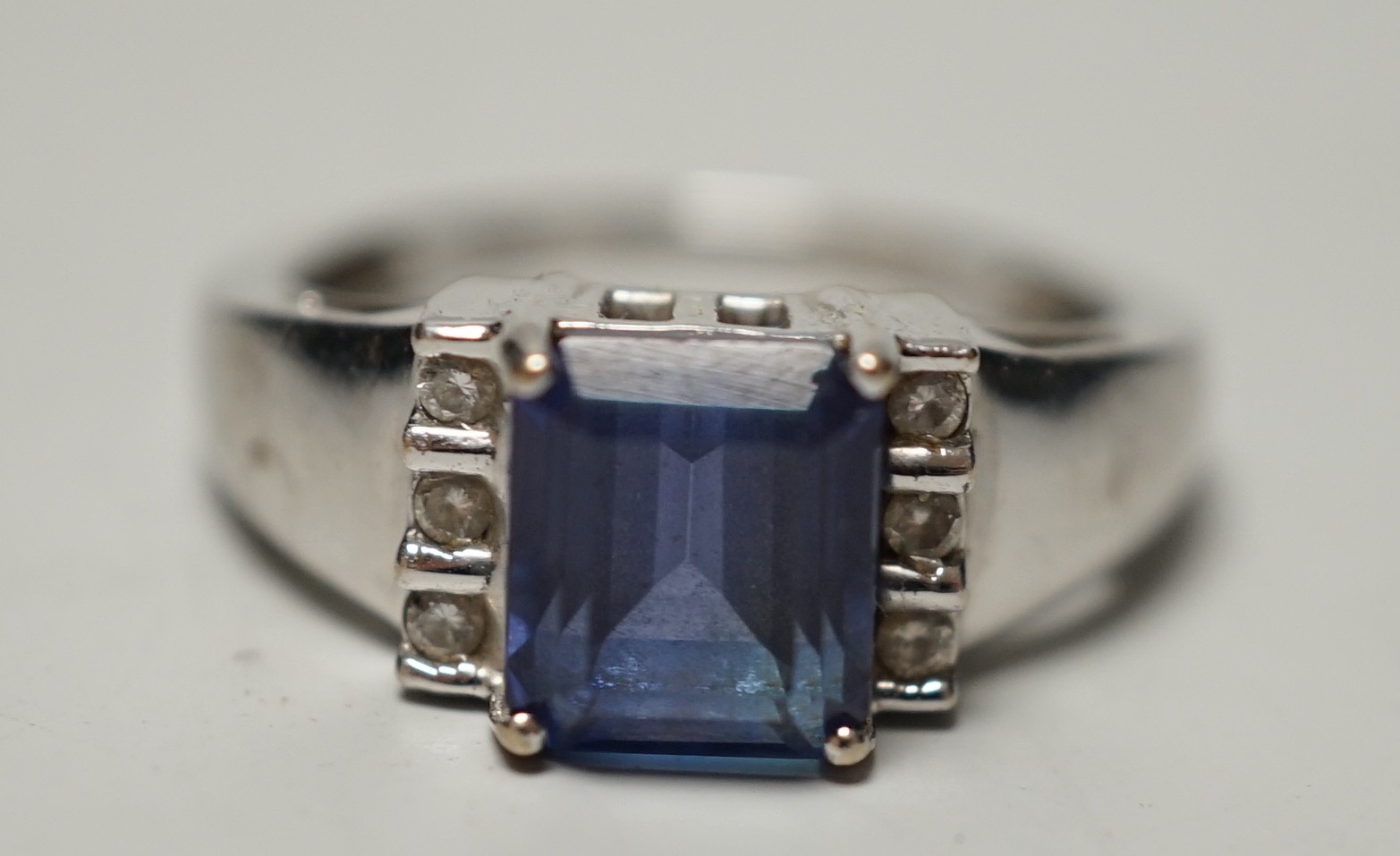 A modern 18k, single stone emerald cut tanzanite and six stone diamond cluster set ring, size O, gross weight 5 grams, with accompanying IGI report dated 6/9/2006.
